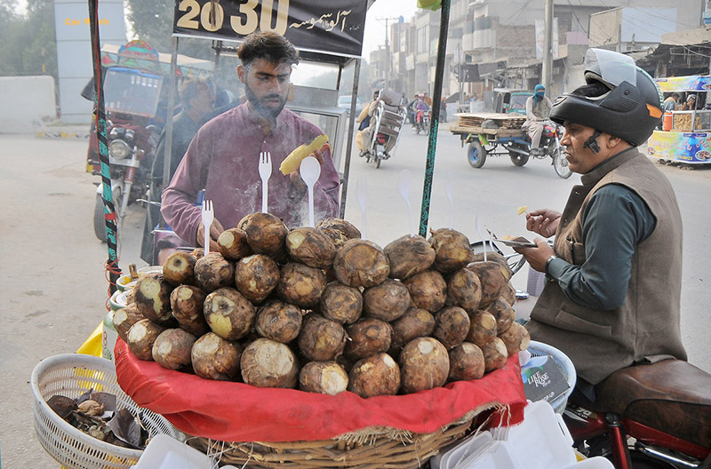 A vendor selling charcoal-roasted sweet potatoes to attract customers at his roadside setup