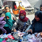 Customers selecting and purchasing second hand warm clothes from the roadside vendors