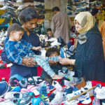 A couple selecting and purchasing second hand shoes for child from vendor at Station Road