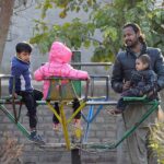 A man with his children playing on a swing at a local park