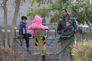 A man with his children playing on a swing at a local park