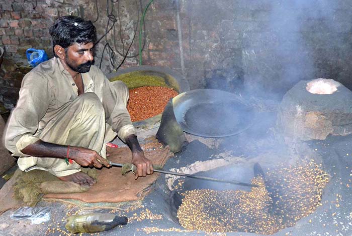 A worker busy in roasting grams for customers at his workplace.