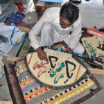 A skilled worker is writing the Qur'anic verse on a hand fan