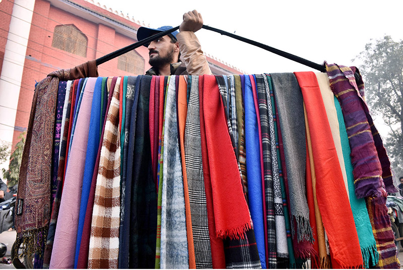 A street vendor carrying the warm winter scarf for selling while shuttling on the road at Landa Bazar