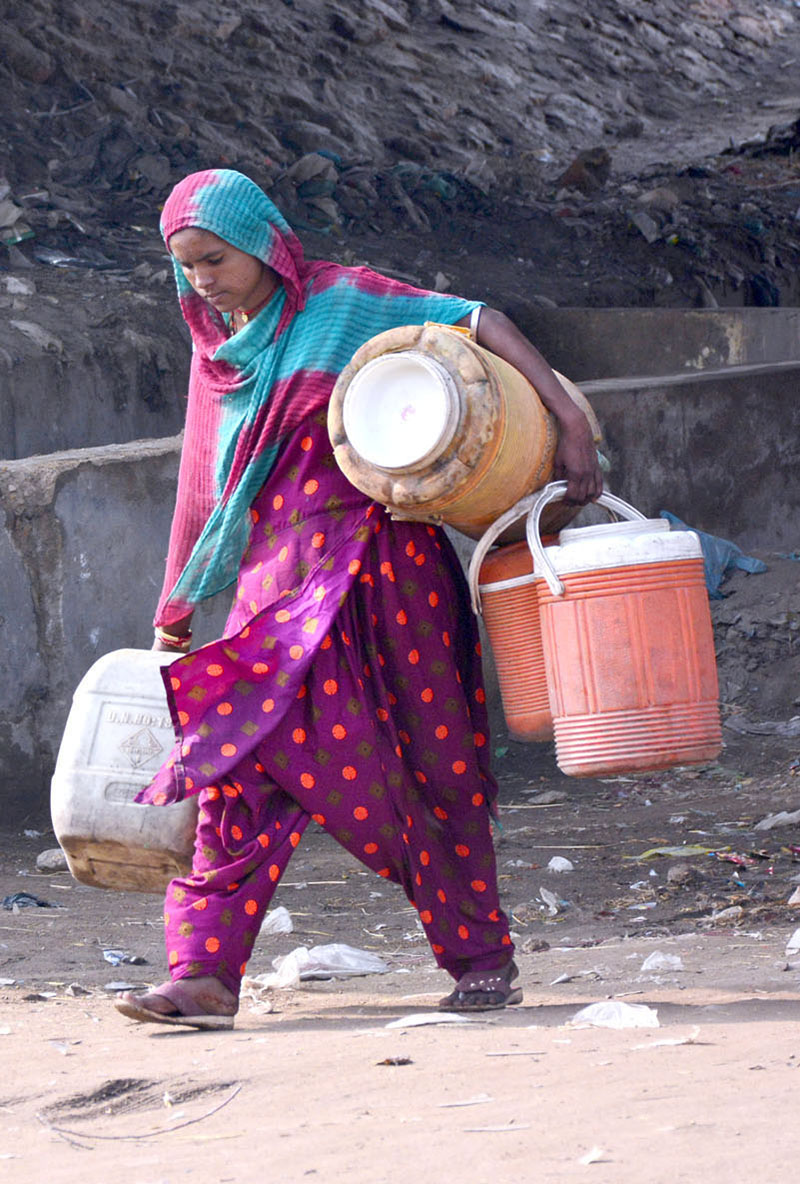 Gypsy woman on the way while carrying pots for filling clean drinking water at Latifabad.