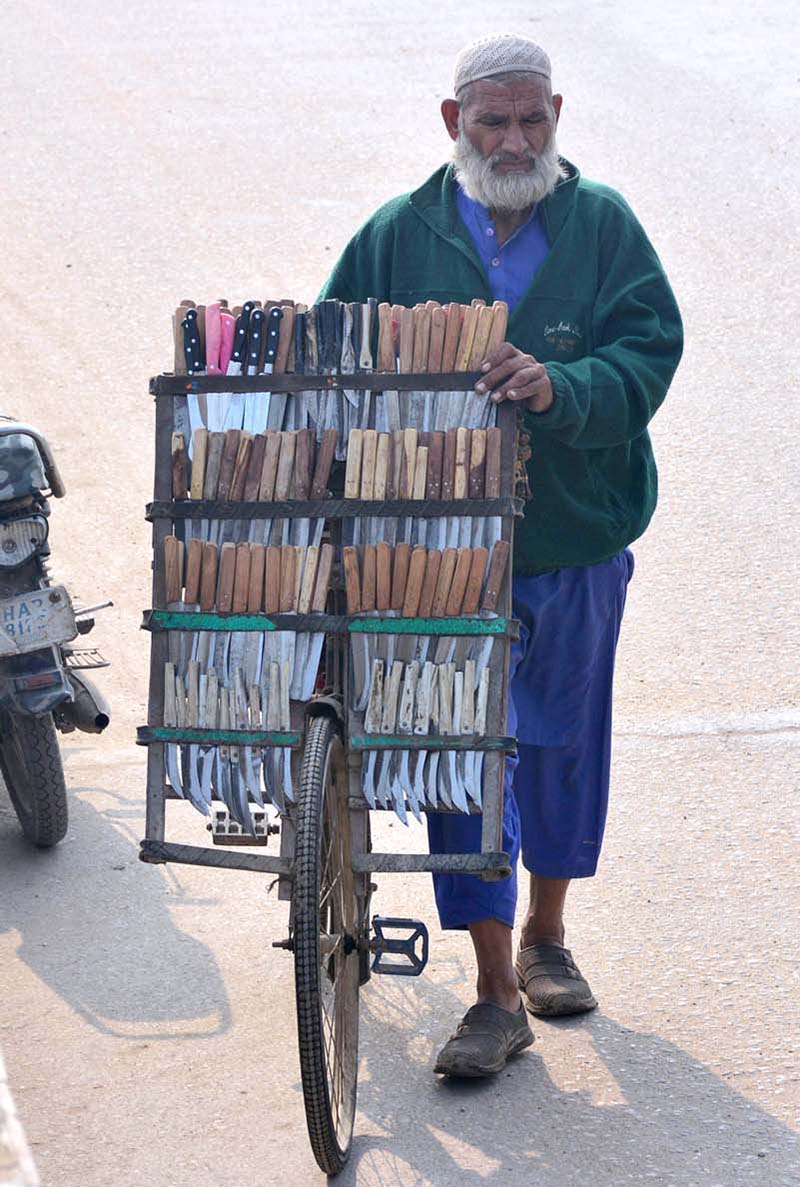 An elderly vendor displaying knives to attract the customers on his bicycle at Subzi Mandi Road