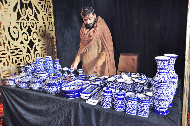 A man arranges various blue pottery items to attract customers at a stall during Lok Mela organized by the Parks and Horticulture Authority