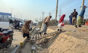 A person holding hand of woman to cross nullah through temporary wooden ladder along road at Pirwadhai.