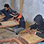 Workers busy in netting wooden chairs at their place in a local market.