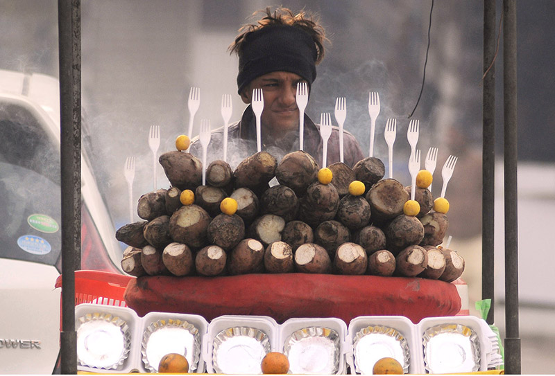 A young vendor selling charcoal-roasted sweet potatoes to attract customers at his roadside setup