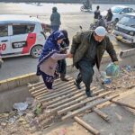 A person holding hand of woman to cross nullah through temporary wooden ladder along road at Pirwadhai.