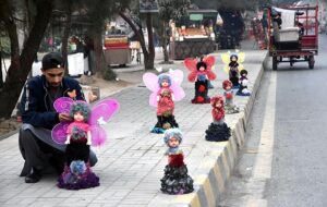 A vendor arranging and displaying dolls to attract the customers on footpath along Murree Road.