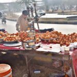 A vendor arranging and displaying oranges for extracting juice at his roadside setup in Federal Capital