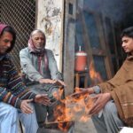 Shopkeepers sitting around fire to keep them warm during cold weather in the Federal Capital.