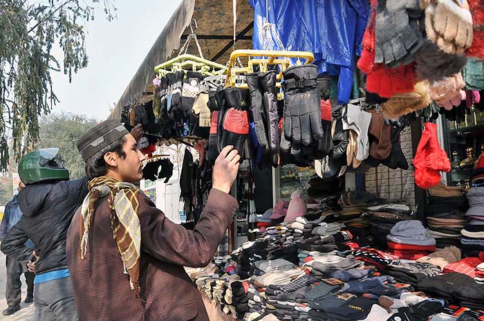 A youngster selecting and purchasing gloves from vendor at Aabpara in Federal Capital.