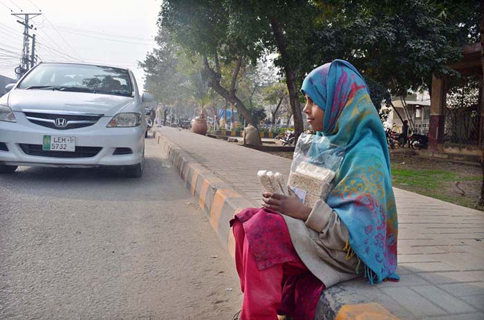 A young girl selling traditional item (Maronda) while sitting ON footpath at Club Road