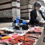 An elderly vendor reading newspaper while waiting for customers to sell different stuff at roadside setup at Aabpara in Federal Capital