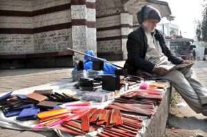 An elderly vendor reading newspaper while waiting for customers to sell different stuff at roadside setup at Aabpara in Federal Capital