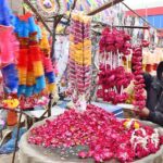 A vendor arranging flower garlands to attract the customers at his roadside setup.