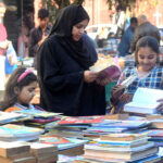 Family selecting and purchasing old books from a roadside setup at Mall Road