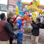 A vendor selling different shapes balloons to customers at roadside vendor