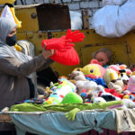A woman selecting and purchasing cloth toys from vendor stall outside road