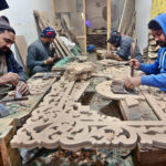 Artisans busy carving design on wooden sheet at his workplace.