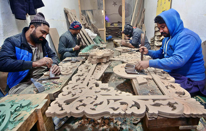 Artisans busy carving design on wooden sheet at his workplace.