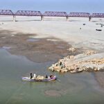 Workers of Irrigation Department shifting stones through boat to the other side of the River.