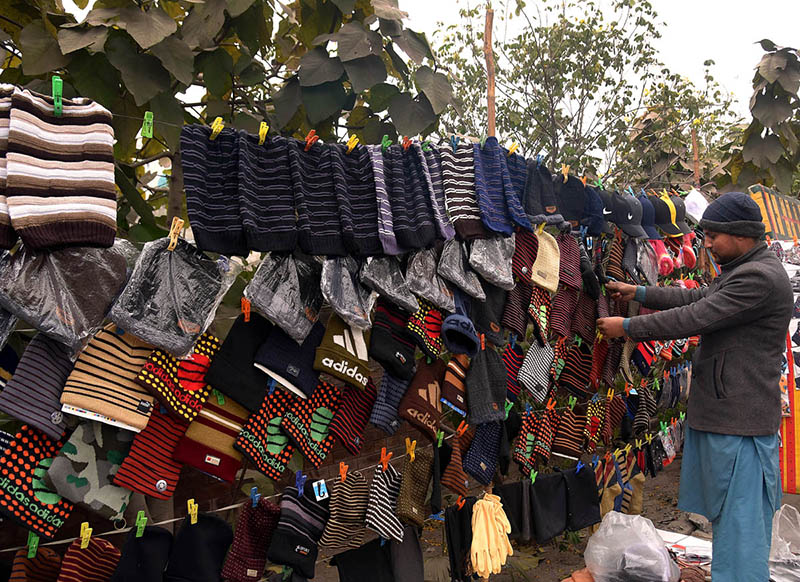 A vendor is busy in displaying and selling Warm hats, scarves and gloves at his roadside setup