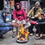 People are sitting around fire during cold weather in the city.