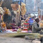 Vendor displaying broom and other household items to attract customers at his roadside setup.