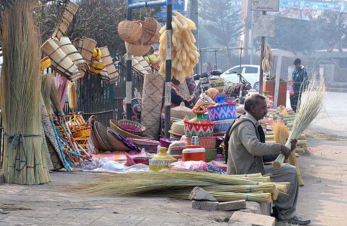Vendor displaying broom and other household items to attract customers at his roadside setup.
