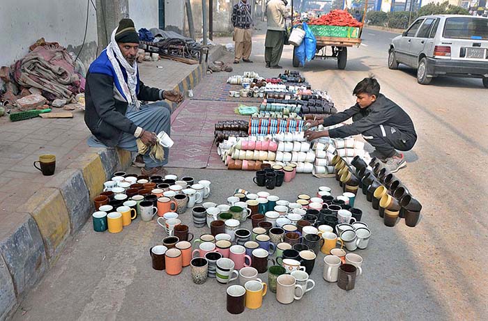 Vendor displaying tea cups to attract customers at roadside setup.