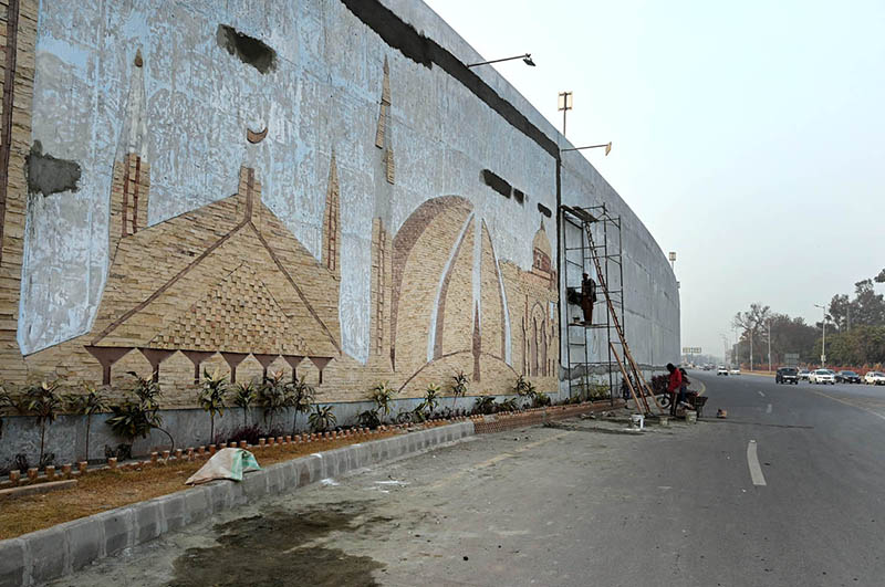 Laborers busy in construction work to enhance the beauty of the city on the wall of a flyover at Rawal Dam Chowk in the Federal Capital