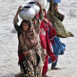 Women on the way back carrying water pots on their head after filling water at bank of Indus River