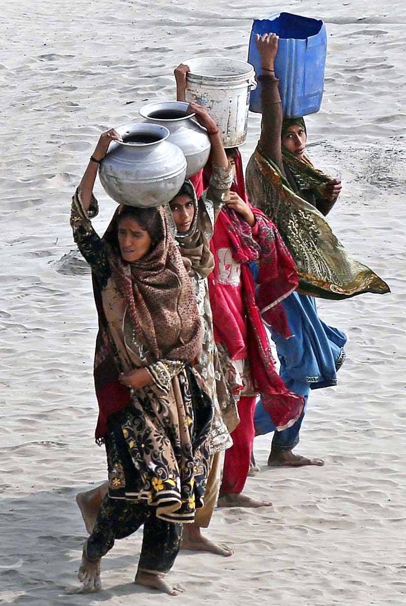 Women on the way back carrying water pots on their head after filling water at bank of Indus River