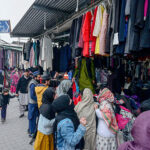Customers selecting and purchasing old clothes displayed by the vendor at weekly Bazaar.