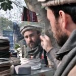 A person selecting and purchasing Chitrali Cap from roadside vendor in Federal Capital