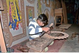 Young artisan busy carving design on wood at his workshop. 