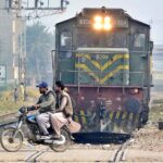 Motorcyclist crossing railway track while train is approaching.