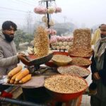 A local vendor roasting corn cob and displaying different items of dry fruits to attract the customers at Ring Road.