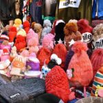 A vendor arranging and displaying the warm winter caps and different warm stuff to the customers on his handcart at local market