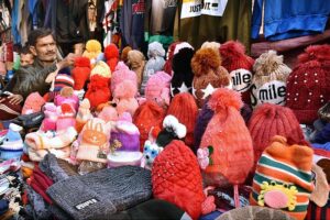 A vendor arranging and displaying the warm winter caps and different warm stuff to the customers on his handcart at local market