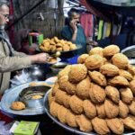 A vendor is busy in making and selling the traditional food item “Laddu Peethi” to the customers on his roadside setup at local market.