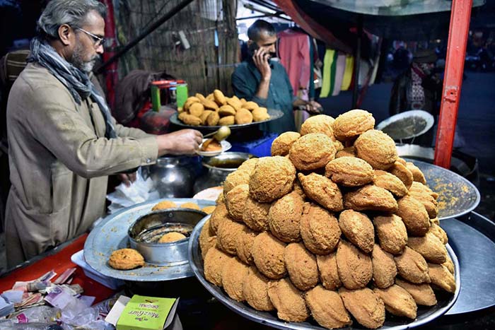 A vendor is busy in making and selling the traditional food item “Laddu Peethi” to the customers on his roadside setup at local market.