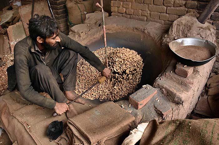 A worker busy in roasting the peanuts for customers at his workplace.