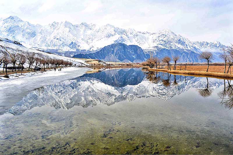 Attractive and eye catching view of reflection of snow covered mountain and leafless tree's in Katpana Desert Lake in the catchment area of Pakistan