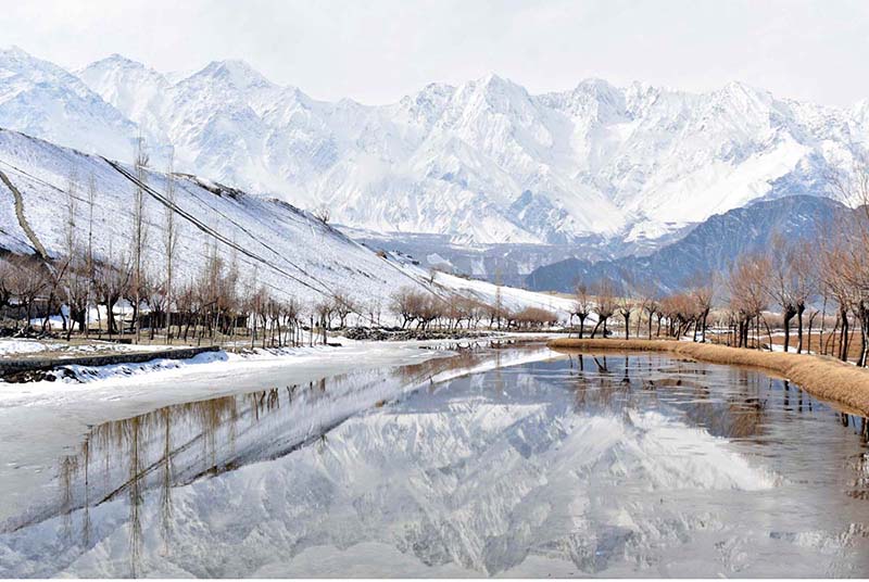 An attractive and eye catching view of reflection of snow covered mountain and leafless tree's in Katpana Desert Lake during the 1st snow fall in the area