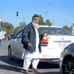 An aged man is selling plastic toys on a busy road.